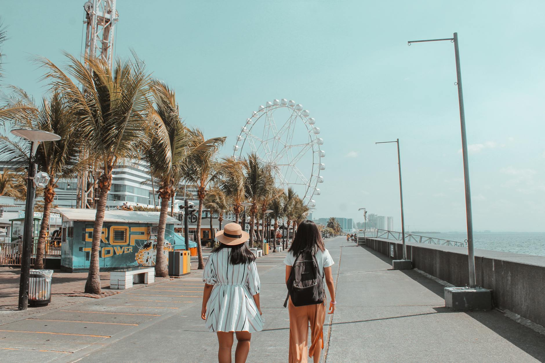 Dwie kobiety spacerują nadmorską promenadą obok diabelskiego młyna