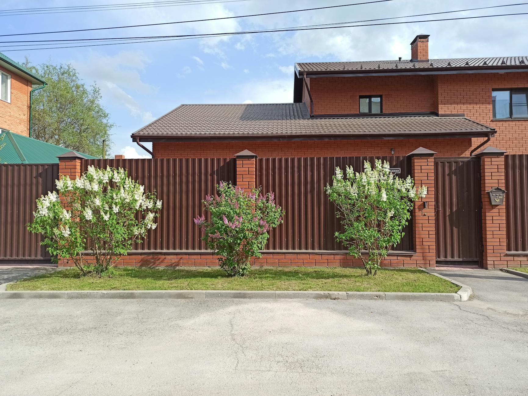 Jak wybrać idealne ogrodzenie do domu: praktyczny poradnik krok po kroku Ceglasty dom z brązowym metalowym ogrodzeniem i kwitnącymi krzewami