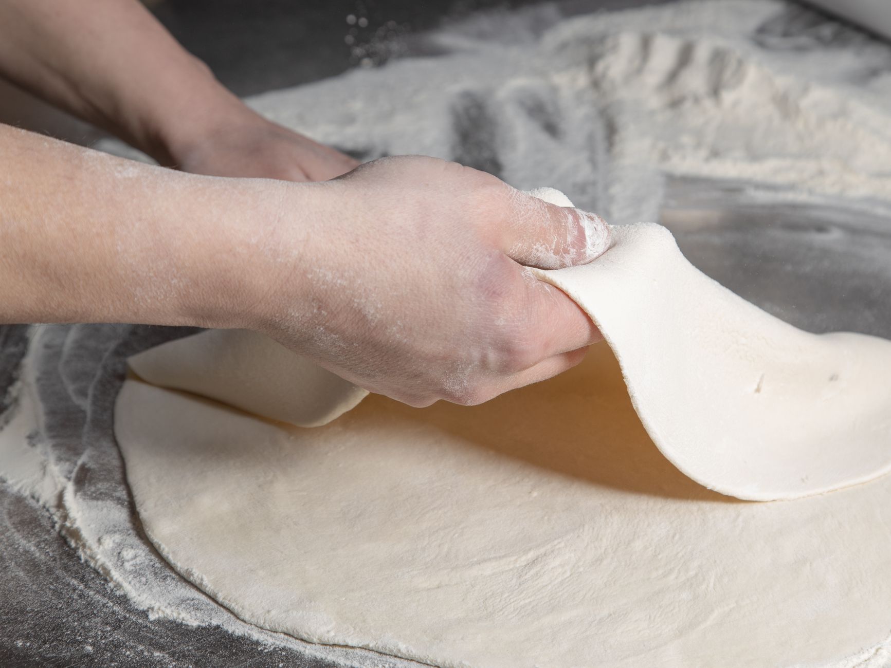 Dłonie wyrabiające ciasto na pizzę na oprószonym mąką blacie