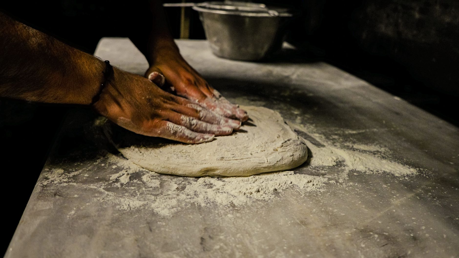 Mężczyzna zagniata ciasto na pizzę na oprószonym mąką blacie Mężczyzna zagniata ciasto na pizzę na oprószonym mąką blacie